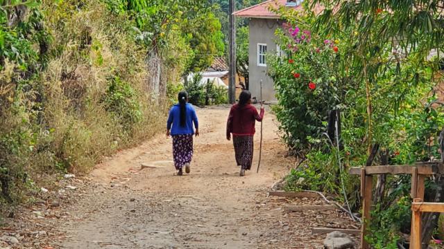 Moradoras da comunidade caminhando de costas por rua de terra