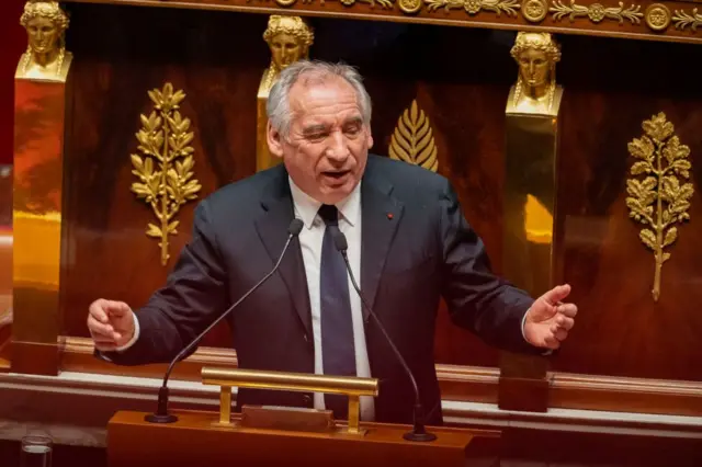 Байру выступает в Национальной ассамблее: он стоит на трибуне и что-то говорит, разводя руками