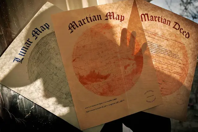 Tres papeles donde se ve el mapa de propiedades de la Luna, el de propiedades de Marte y un tercer papel de las escrituras de una propiedad en Marte.