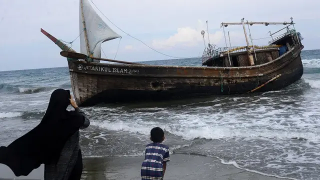 Warga menyaksikan kapal kayu menggunakan layar yang mengangkut puluhan imigran etnis Rohingya terdampar di pantai Desa Ladong, Kabupaten Aceh Besar, Aceh, Minggu (25/12/2022).