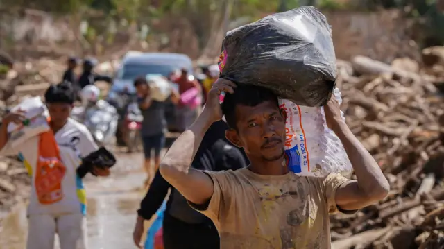 Warga melintasi jalan akses antardesa pascabanjir bandang di Desa Tanjung Karang, Karang Baru, Kabupaten Aceh Tamiang, Aceh, Minggu (7/12/2025). Akses penghubung Desa Tanjung Karang dan Desa Menang Gini yang sempat tertutup tumpukan kayu gelondongan akhirnya bisa terbuka usai pemerintah mengerahkan alat berat untuk pembersihan sehingga mobilitas masyarakat, termasuk distribusi bantuan menjadi bisa dilakukan. 
