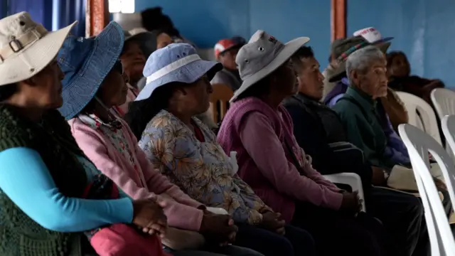 Varias mujeres están sentadas prestando atención a una charla que se está dando en el pueblo. 