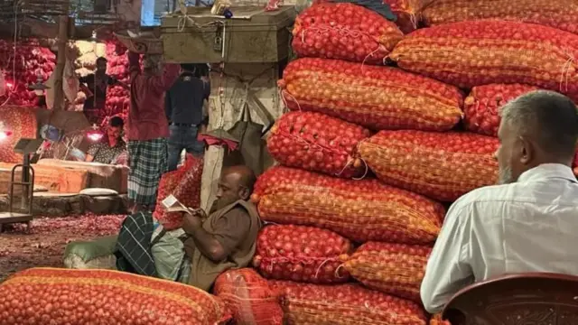 কারওয়ান বাজারে পেঁয়াজের আড়তে স্বচ্ছ সারি সারি বস্তায় পেঁয়াজ রাখা, পাশে বসে আছেন কয়েকজন ব্যবসায়ী