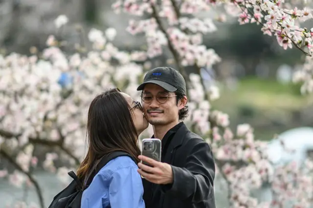 Dos personas se toman una selfie con unos cerezos de fondo