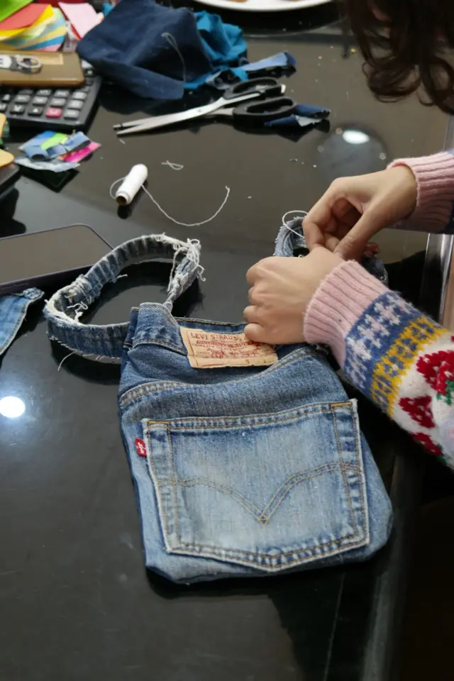 जीन्सको कपडा र सिउन लागेकी एक महिलाको हात