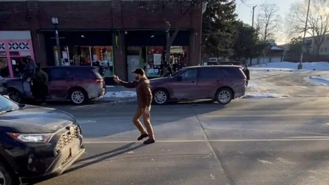 Скриншот из видео, полученного агентством Reuters, показывает мужчину, идентифицированного как Алекс Претти, снимающего что-то на мобильный телефон, стоя на проезжей части. Что он снимает, остается за кадром