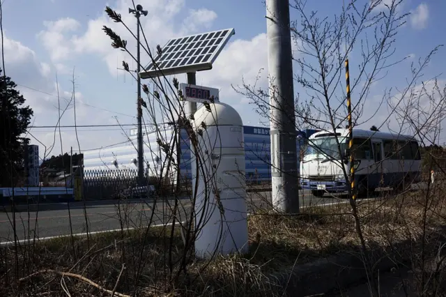 Üzerinde güneş paneli olan bir radyasyon ölçüm istasyonu. Cihazın arkasındaki yolda ilerleyen bir araç görünüyor. 