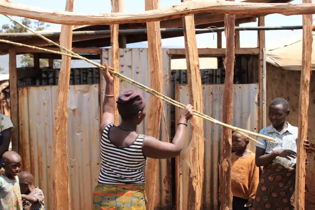 Une femme et des enfants construisant une maison dans le camp