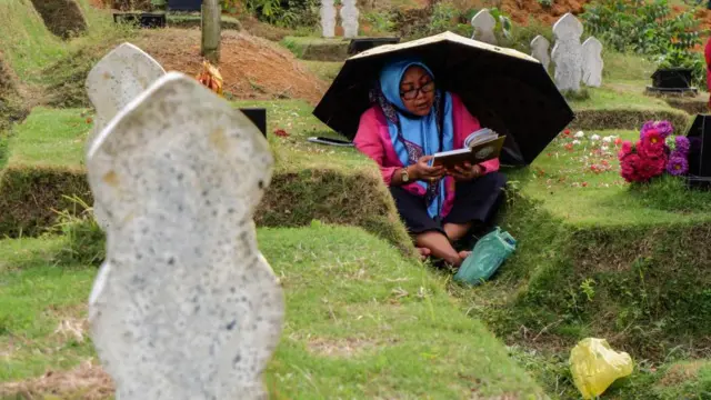 Seorang ibu membaca Al-Qur'an di pemakaman korban COVID-19 di Medan, Minggu (19/03). 