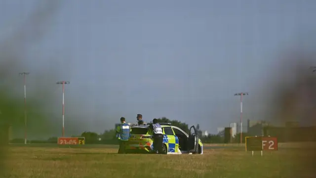 Поліцейська машина біля злітно-посадкової смуги, а на землі стоять знаки F2 і F1.