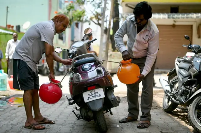 दो पहिया गाड़ी में पानी लेकर जाते हुए लोग