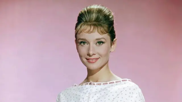 Audrey Hepburn, pembe bir duvarın önünde kameraya bakıyor