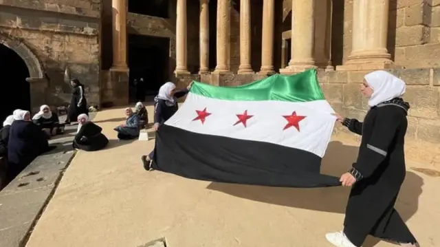 Wanawake wanatazama bendera mpya ya Syria, inayotumiwa na upinzani, ikipeperushwa
