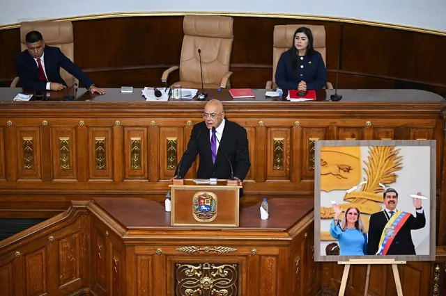 Jorge Rodriguez yeniden Ulusal Meclis'in başkanı seçildi. Rodriguez konuşma yaparken yanında Maduro ve eşinin fotoğrafı görülüyor.