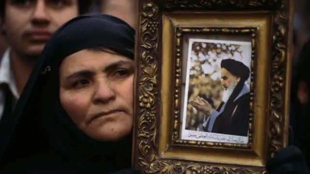 Женщина в хиджабе держит портрет аятоллы Хомейни