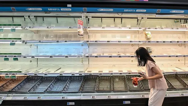 Žena stoji sa kesom crnog luka ispred prazne police u supermarketu