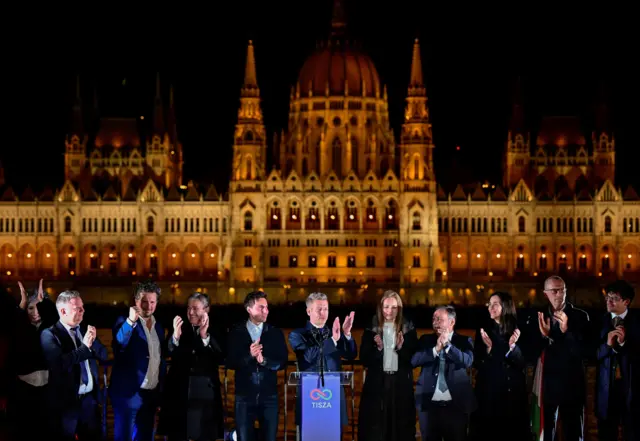 Tisza Partisi lideri Peter Magyar, parti yetkilileriyle birlikte, zafer konuşması için sahnede. Arkada Macaristan Parlamentosu görülüyor. 12 Nisan 2026. 