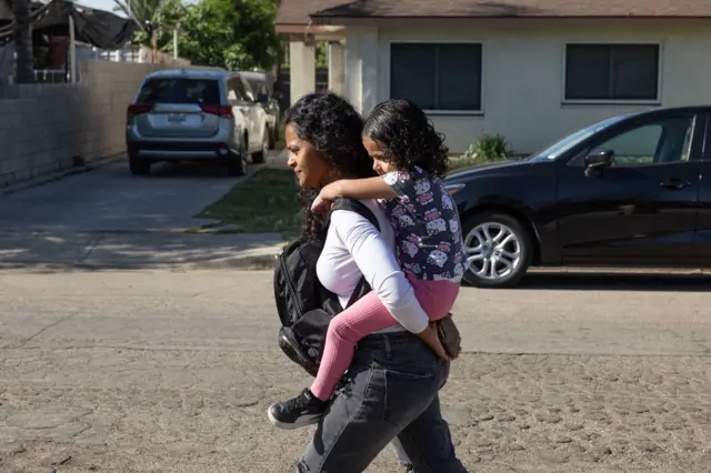 Deysi Vargas carga a su hija Sofía (seudónimo) hasta su escuela en Bakersfield, California, Estados Unidos, el viernes 23 de mayo de 2025. (Myung J. Chun / Los Angeles Times a través de Getty Images).
