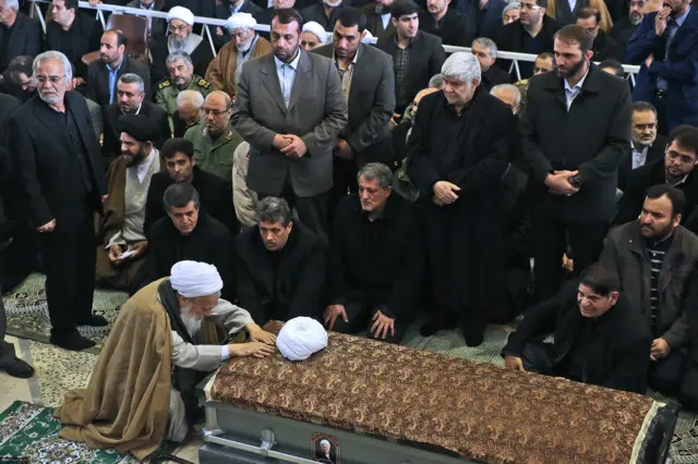 محمدعلی موحدی کرمانی کنار پیکر آقای هاشمی دعا می‌خواند. در کنار او به ترتیب از چپ فرزندان آقای هاشمی نشسته‌اند: یاسر، مهدی و محسن هاشمی