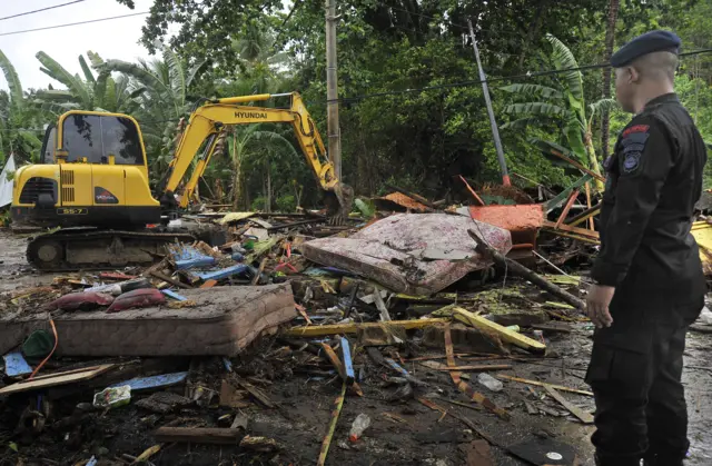 Petugas mengawasi operator alat berat membersihkan tumpukan sampah yang porak poranda menutupi jalan setelah diterjang tsunami di Pantai Carita, Pandeglang, Banten, Minggu (23/12/2018).