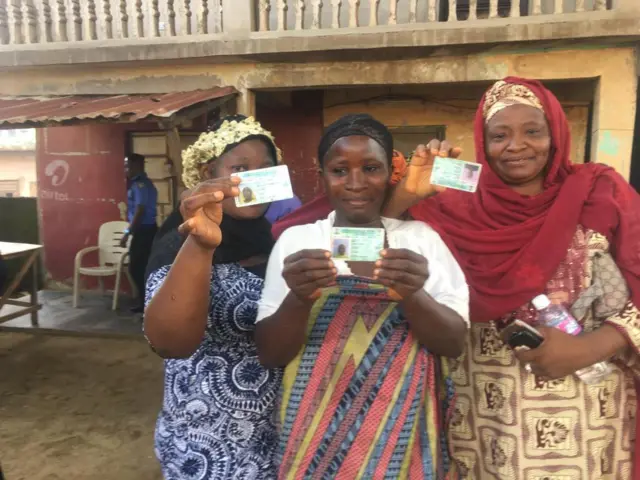 three women dey show off dia voters card