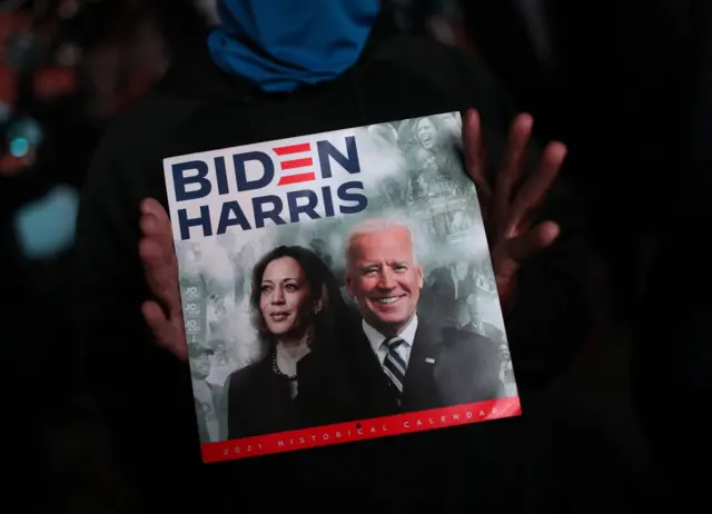 Un partisan du président nouvellement élu Joe Biden montre un calendrier avec Biden et le vice-président élu Kamala Harris en couverture devant le Chase Center où Biden s'est adressé à la nation le 7 novembre 2020 à Wilmington, Delaware.