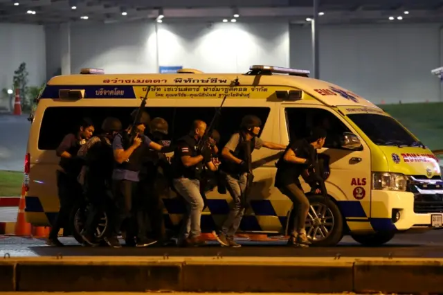 Thailand security forces take cover behind an ambulance as they chase a shooter hidden in a shopping mall after a mass shooting in front of the Terminal 21