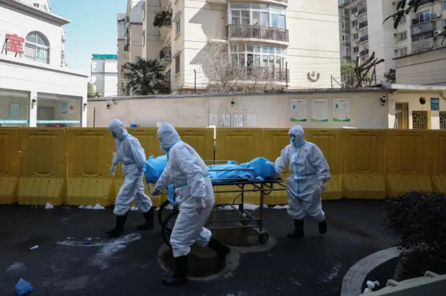 Workers move the body of a COVID-19 victim