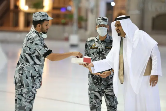 Suudi Arabistan'da da Ramazan Bayramı sokağa çıkma kısıtlamaları altında kutlanıyor, Mekke Büyük Camii'nde bir kişi güvenlik güçlerine tatlı ikram ediyor