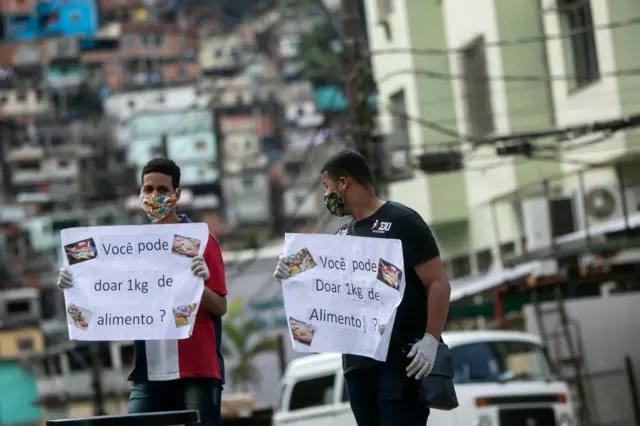 Rio de Janeiro'nun kenar mahallelerinde "1kg yiyecek bağışlar mısınız?" yazısı tutan gençler.