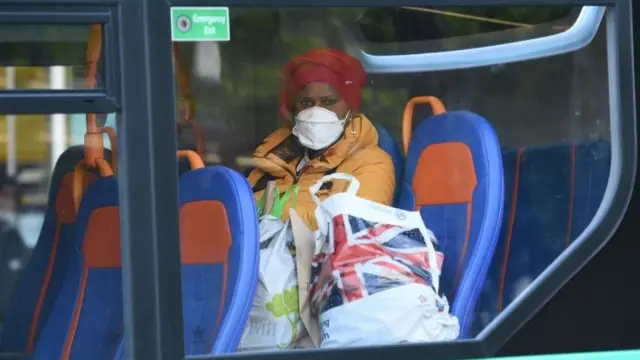 ब्रिटेन में कोरोना वायरस से बचाव के लिए मास्क लगाकर बस में सवारी करती हुई एक महिला