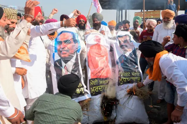 पीएम मोदी, कारोबारी मुकेश अंबानी और अडानी का पुतला जलाते लोग