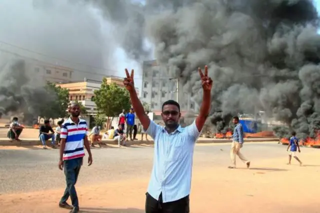 Wani daga cikin masu zanga-zanga yana nuna alamar nasara a kusa da inda tayoyi ke cin wuta