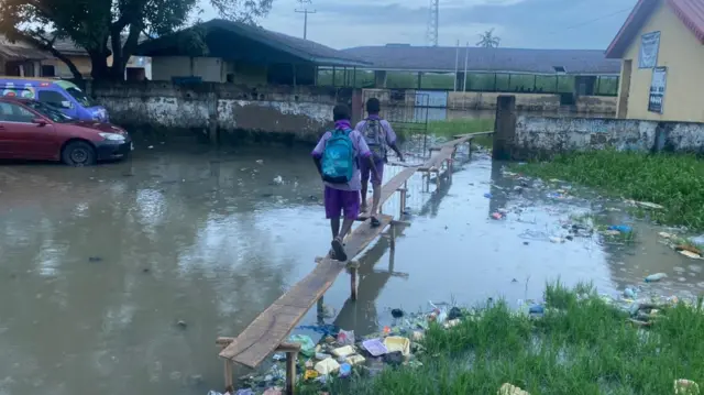 Two school boys dey walk on wooden bridge