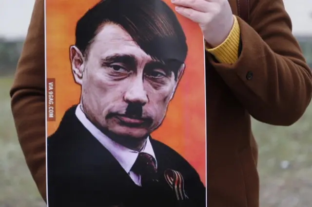 A person holds a placard showing Vladimir Putin dressed as Adolf Hitler as people protest against Russia"s military operation in Ukraine, outside the Russian Embassy in Riga, Latvia, 24 February 2022.