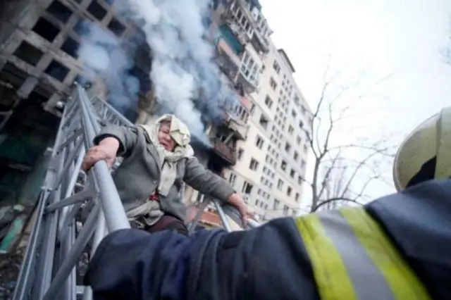 In the capital Kyiv, where Russian troops fight to gain a foothold, a woman is rescued from her home after the building was struck by shelling