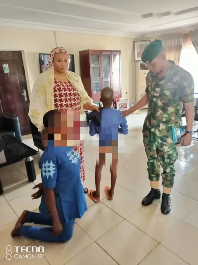 One woman kneel down for ground while one soja and anoda woman dey stand wit one boy