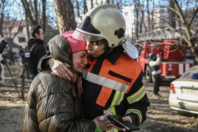 Спасатели успокаивают женщину, эвакуированную из многоквартирного дома в Киеве, подвергшегося российским обстрелам