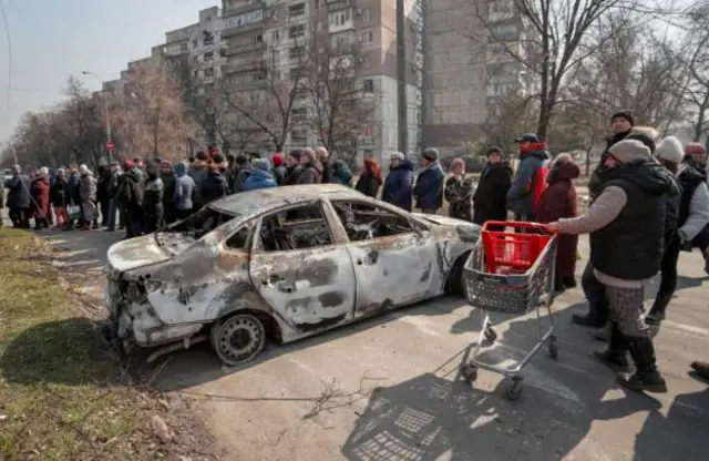 Dozens of Ukrainians queue for food and other supplies in a Russian-controlled part of Mariupol