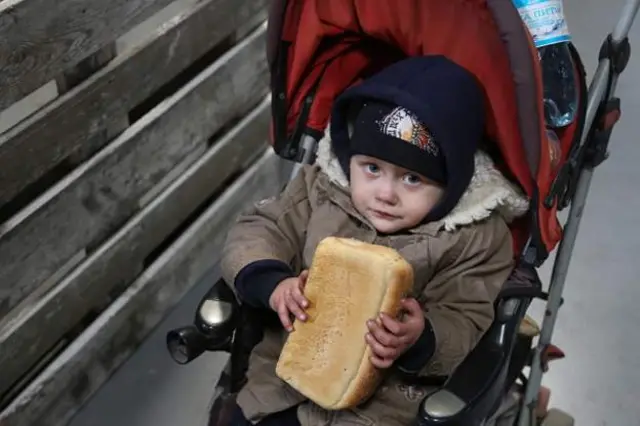 Một em bé cầm bánh mì khi đang được sơ tán theo các hành lang nhân đạo từ Mariupol