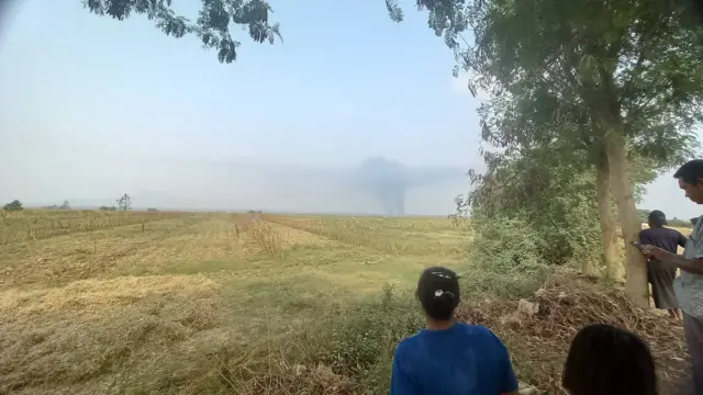 ရွာထဲကတက်လာတဲ့မီးခိုးလုံးတွေကို ‌အ‌‌ဝေးကနေကြည့်နေကြတဲ့ နတ်ချောင်းရွာသူရွာသားတွေ