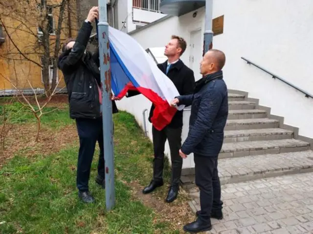 Трое чешских дипломатов поднимают флаг перед зданием посольства в Киеве