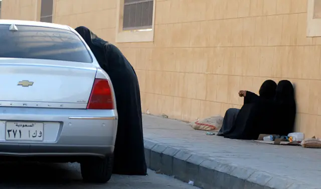 A Saudi man hands money to a woman begging outside a supermarket on a main street in the Saudi capital Riyadh