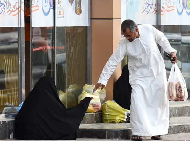 A Saudi man hands money to a woman begging outside a supermarket on a main street in the Saudi capital Riyadh