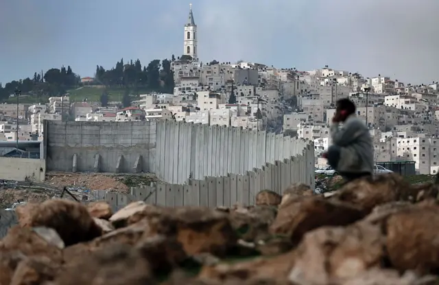 رجل فلسطيني يجلس بالقرب من الجدار الفاصل الإسرائيلي الذي يقسم حي الطور الفلسطيني في القدس الشرقية التي ضمتها إسرائيل إلى الضفة الغربية.