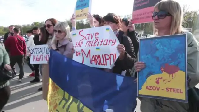 Мирні жителі тримають таблички із проханням безпечного виведення українських військових, які залишаються в пастці під металургійним заводом