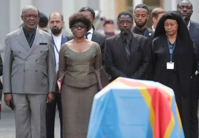 Roland, Juliana na Francois Lumumba, watoto wa marehemu Patrice Lumumba wakiwa wamesimama mbele ya jeneza kwenye sherehe iliyofanyika Brussels.