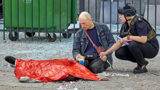 Сотрудница полиции успокаивает мужчину у трупа 13-летнего мальчика, погибшего в результате российского обстрела