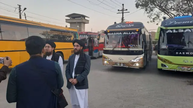 سردار محمد شکیب، دیپلمات طالبان در کنار اتوبوس‌هایی که مهاجران آزادشده از بازداشت را به افغانستان انتقال می‌دهند