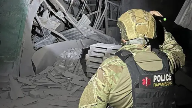 украинский медик на фоне разрушенного дома